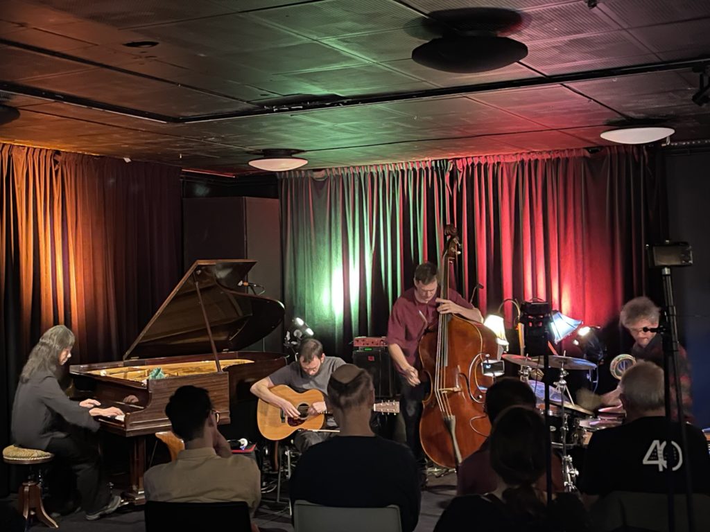 Fyra jazzmusiker spelar på scenen samtidigt som publiken lyssnar noggrant. Det är bandet kommun som spelar.